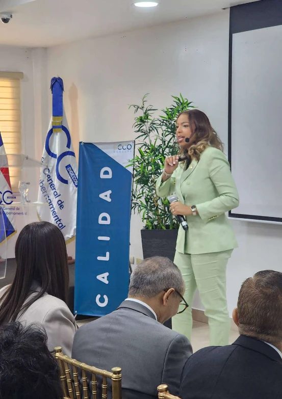 Facilitadora de ECCO Academy presentando frente a un auditorio, junto a un banner de calidad